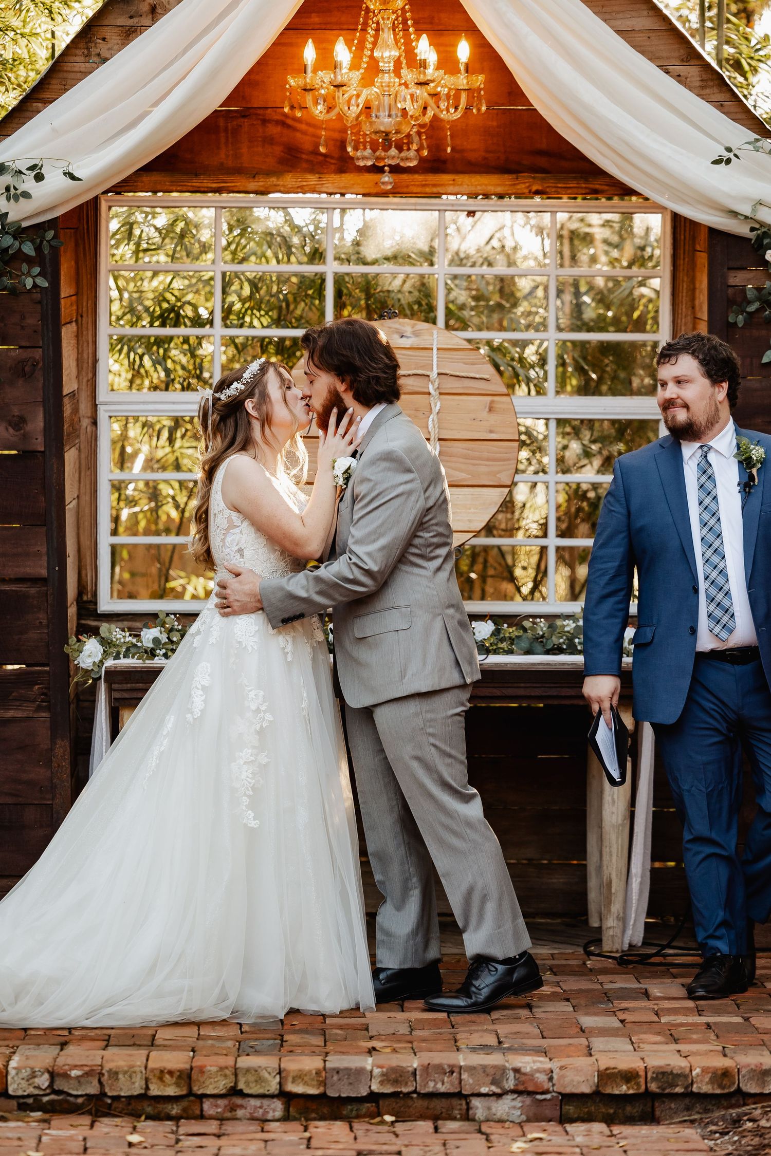 First kiss moment at rustic wooden chapel with elegant chandelier and white draping.
