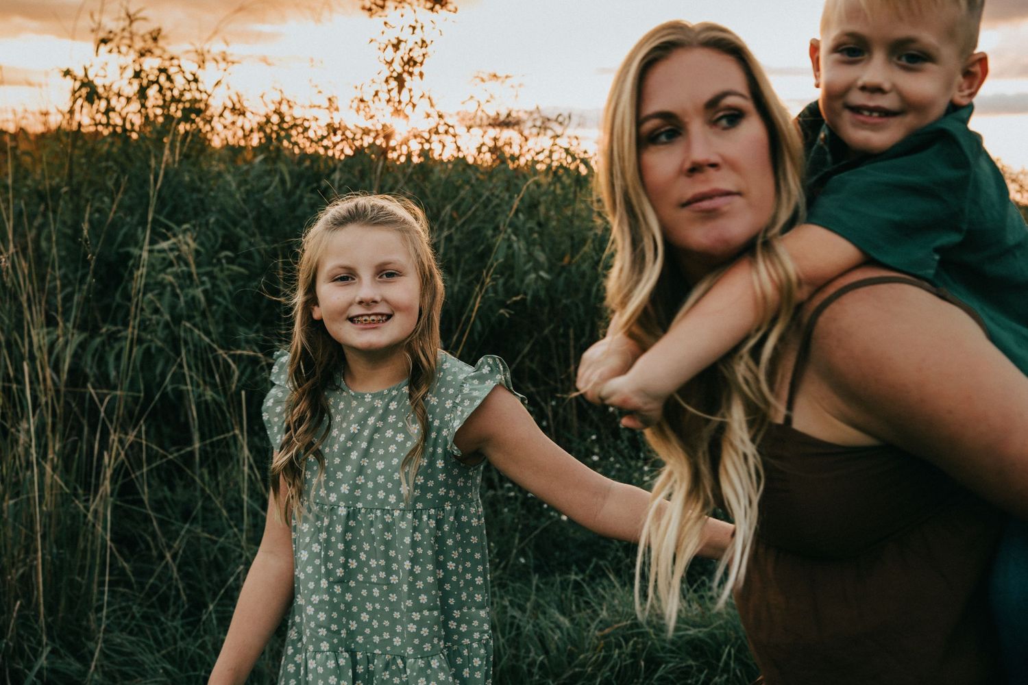 Family of three posing together during sunset in a natural outdoor setting.
