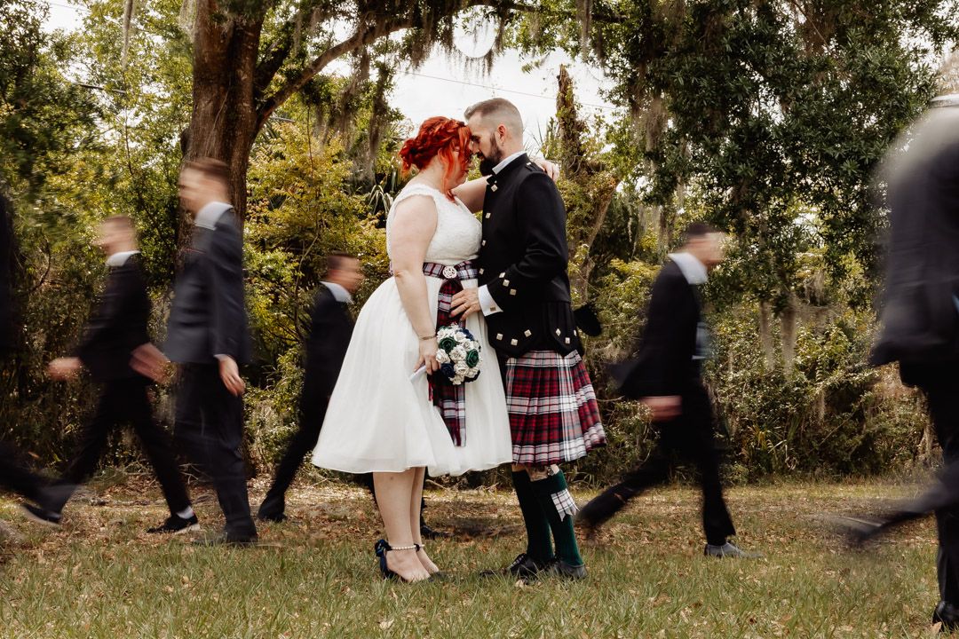 Wedding couple embracing outdoors while people walk past in motion blur.