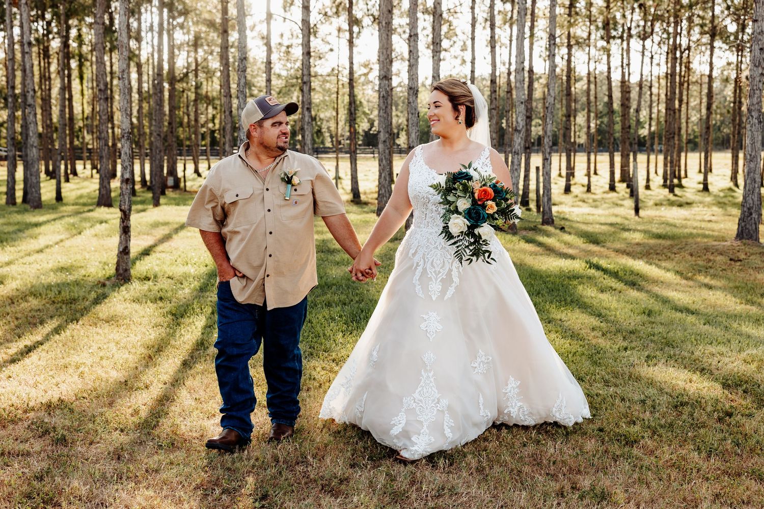 A couple walking hand in hand through a sunlit forest in wedding attire.
