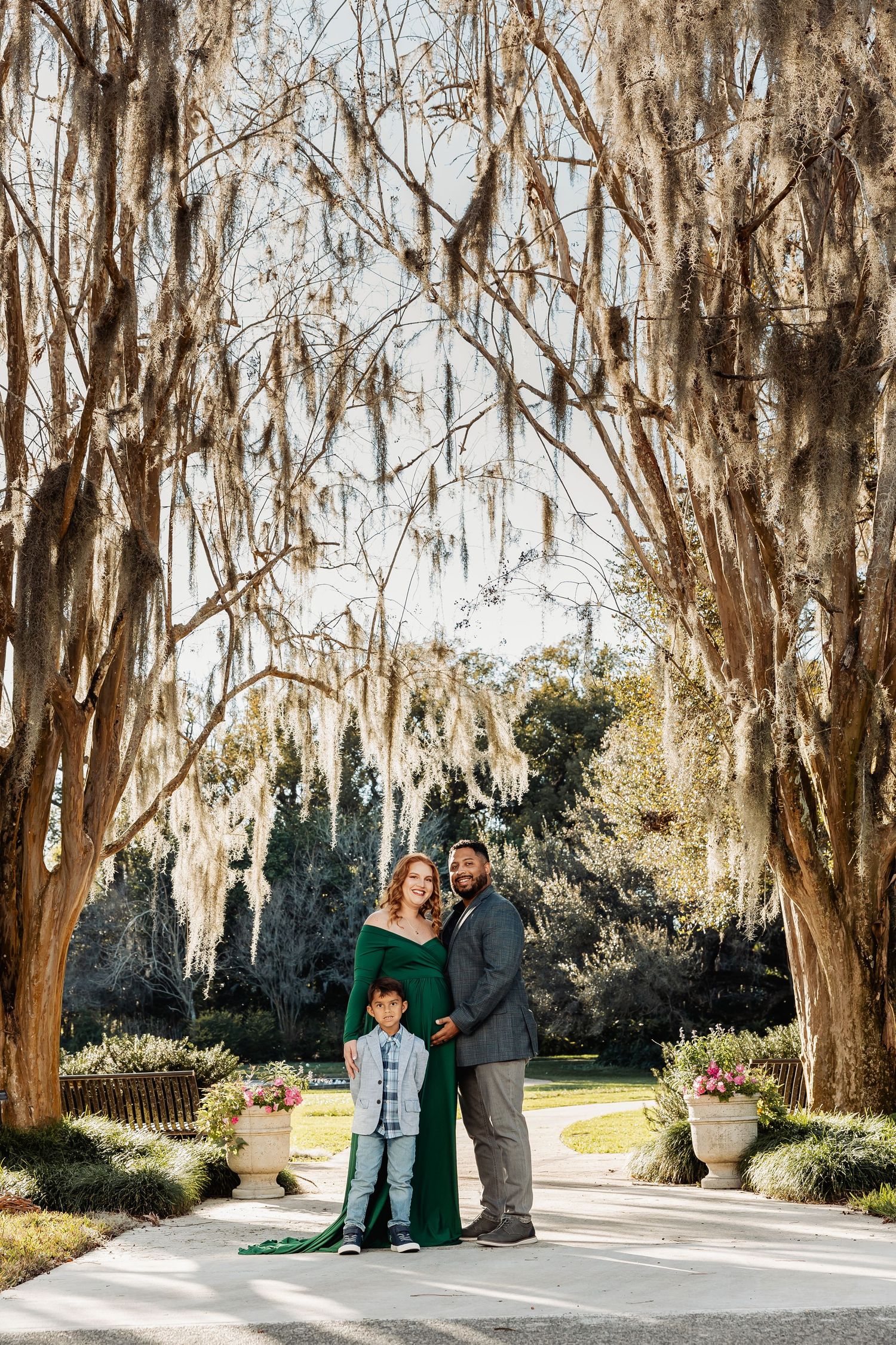 Family maternity photo with pregnant woman in green gown under moss-draped trees.