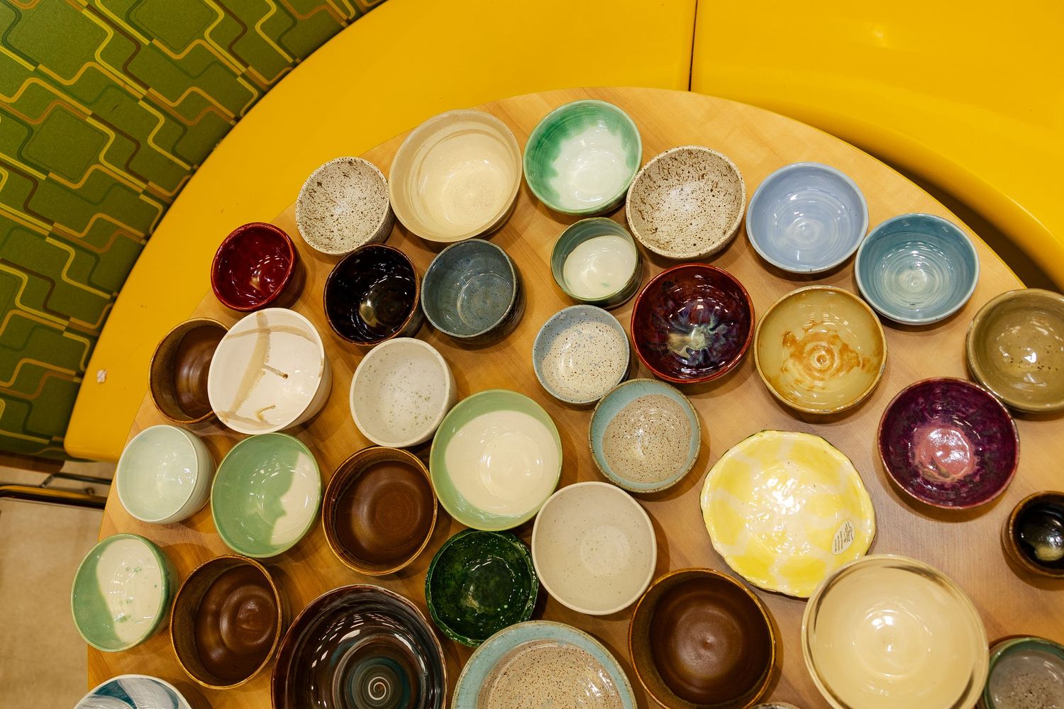 Overhead view of assorted handcrafted ceramic bowls arranged on a yellow circular table.