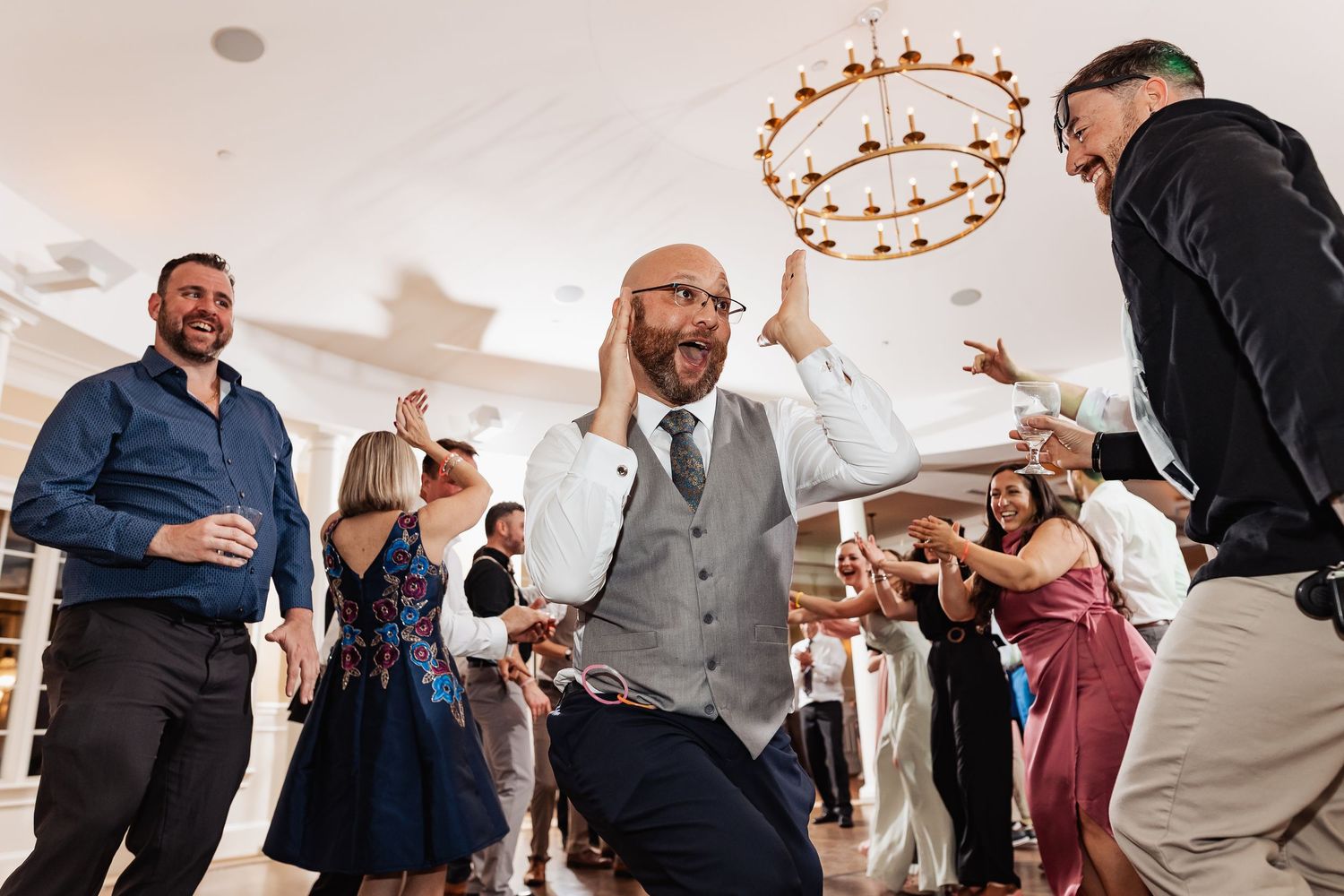 Groom celebrates energetically on the dance floor surrounded by cheering wedding guests at reception.