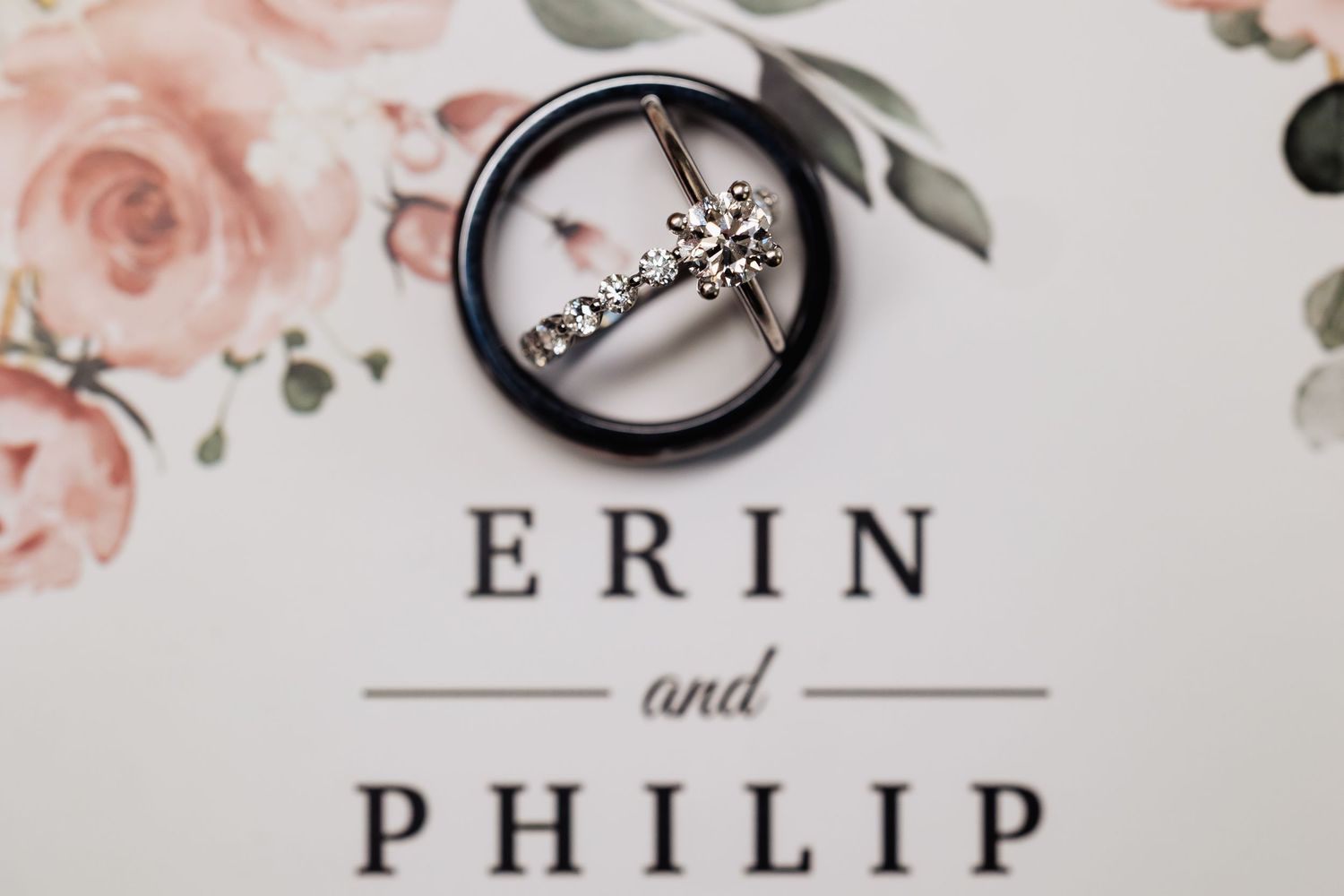 Wedding rings resting on a floral invitation card reading Erin and Philip.