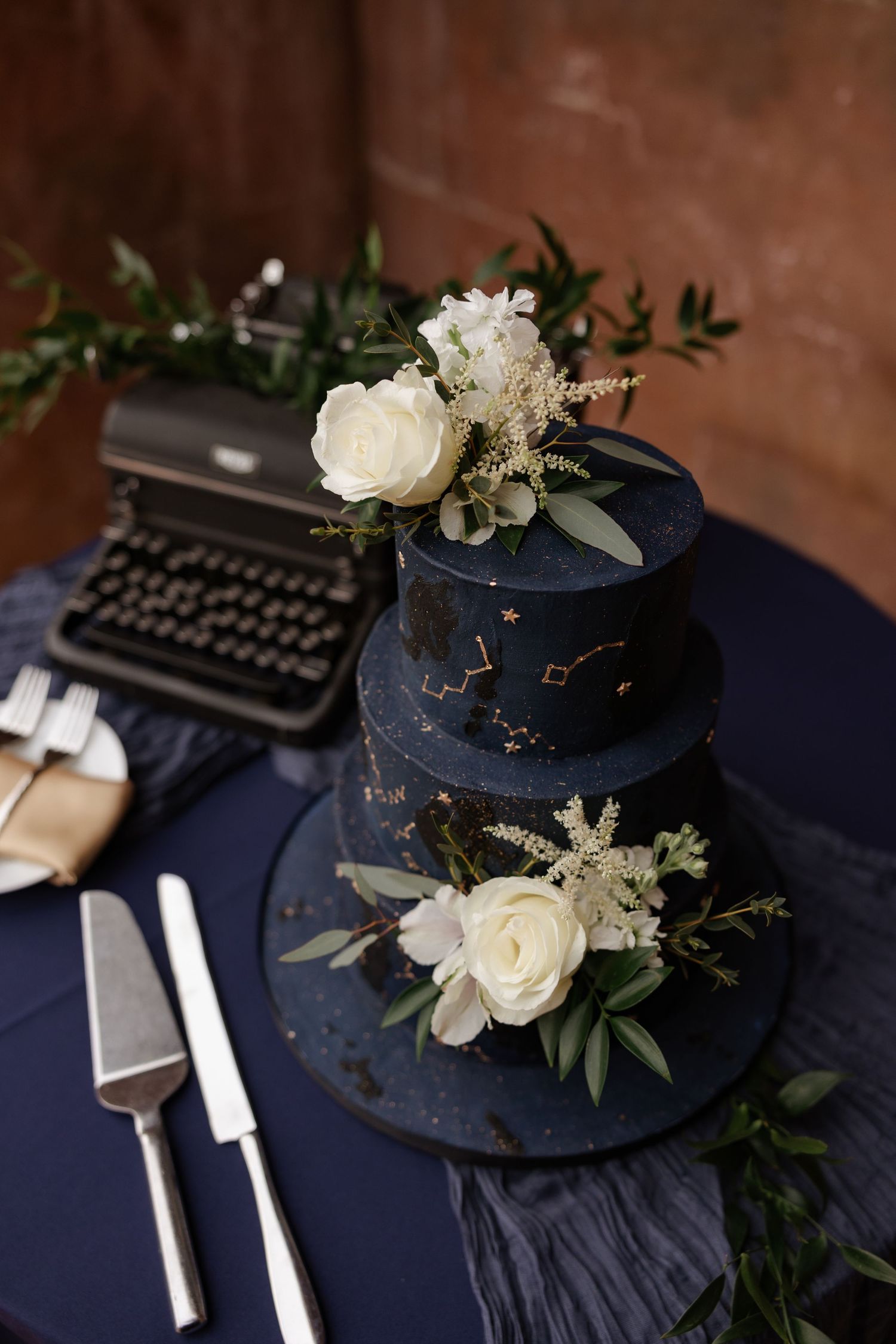 Three-tier navy blue celestial wedding cake with white roses and typewriter.