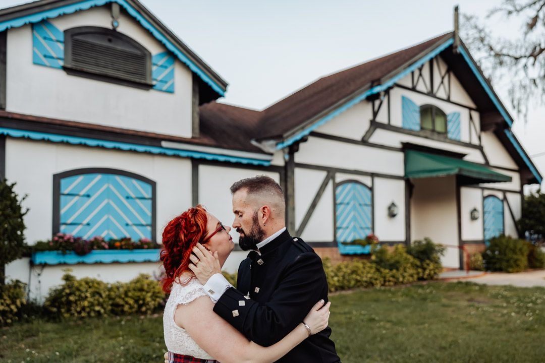 Wedding couple embracing romantically in front of white Tudor-style venue building.