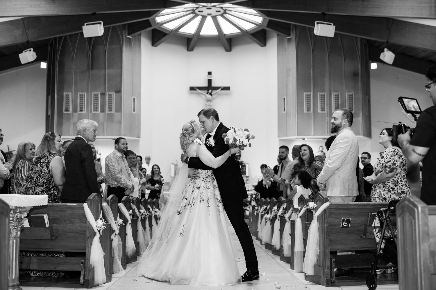 Black and white photo of groom dipping bride for kiss in church aisle after ceremony.