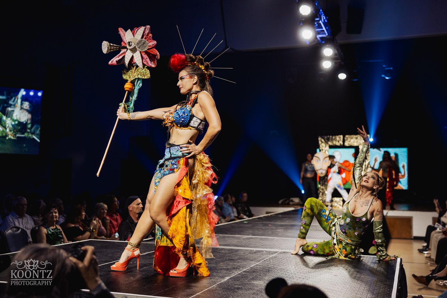 Theatrical dance performance with colorful costumes and dramatic poses under blue stage lighting.
