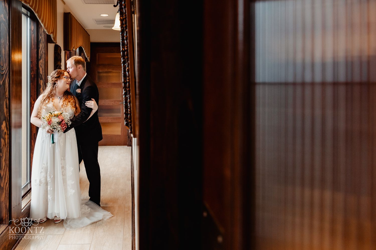Artistic wedding photo captured through a dark wooden doorframe.