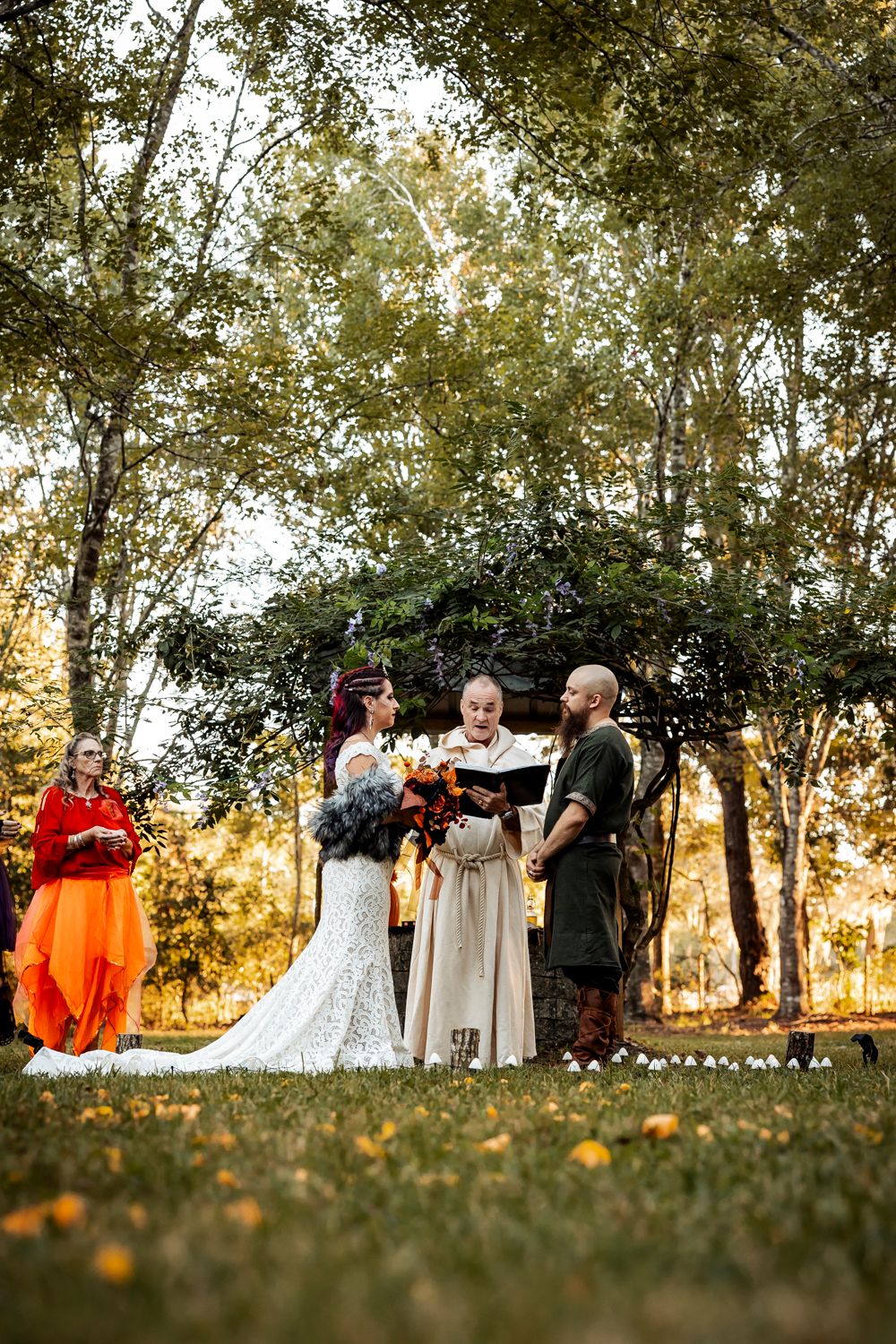 An autumn outdoor wedding ceremony takes place among golden trees at sunset.