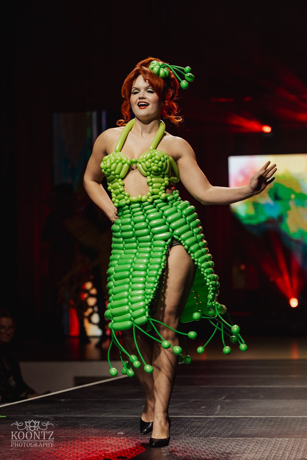 Fashion model walks runway in dramatic lime green balloon-inspired dress with theatrical lighting effects.