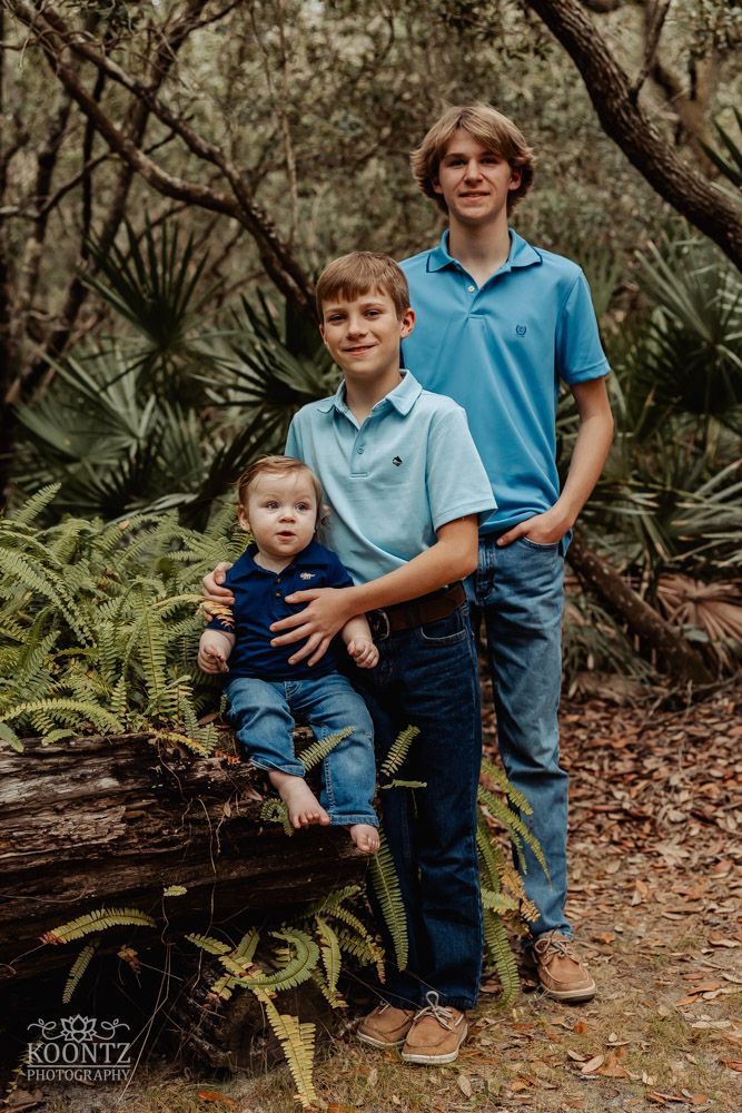 Three people posed together on a nature trail with palm trees and ferns in the background.