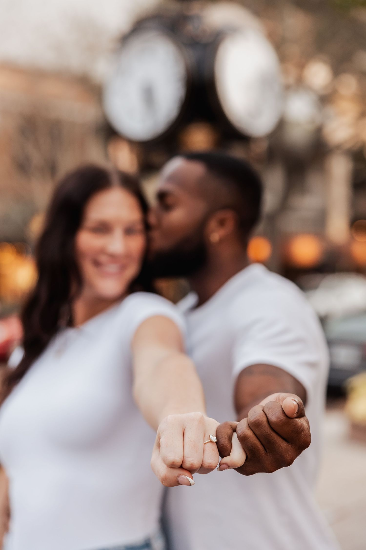 Close-up of intertwined hands with a blurred romantic moment in the background.