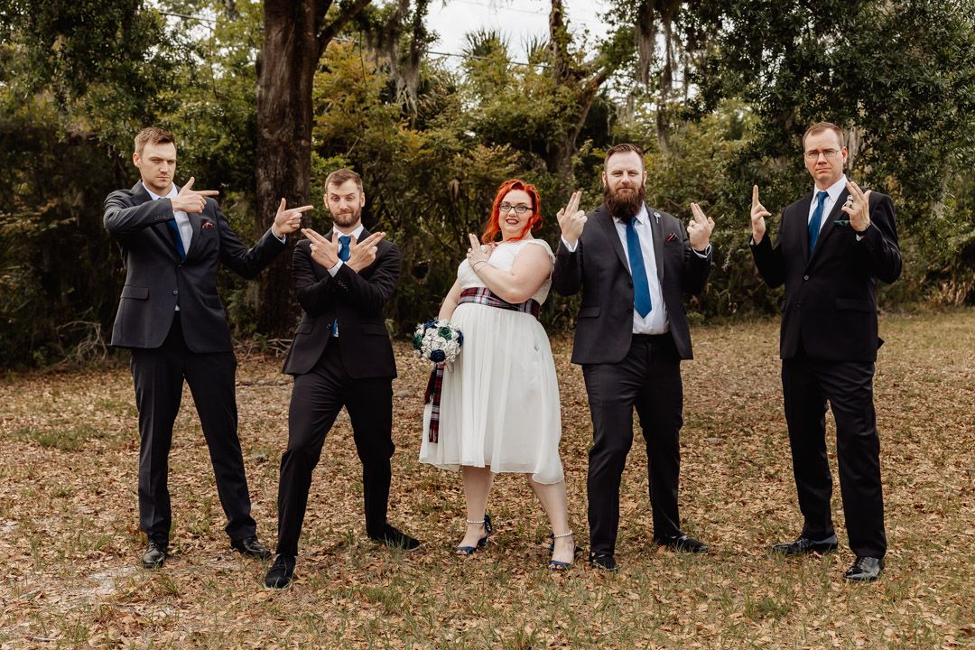 Fun wedding party photo with groomsmen striking dramatic poses outdoors.