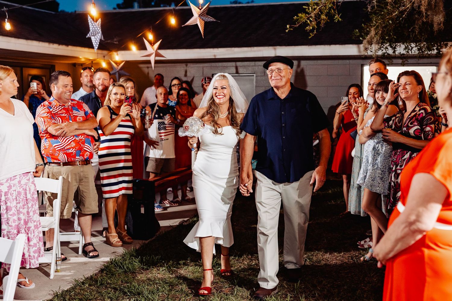 Bride and groom walking through cheering guests at outdoor backyard patriotic wedding reception.