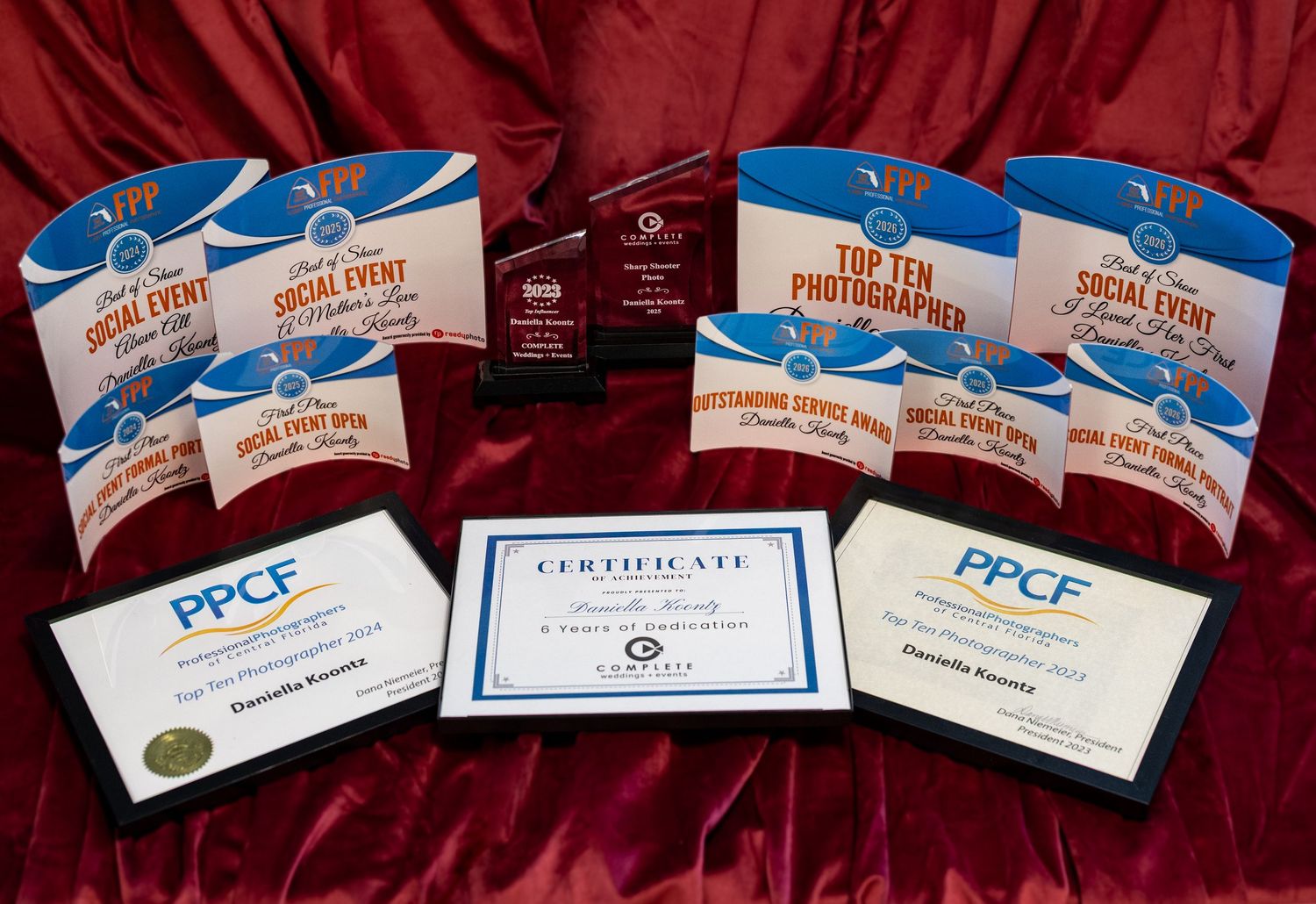 Multiple photography awards and certificates displayed on red fabric, including PPCF plaques and Social Event Photographer trophies.