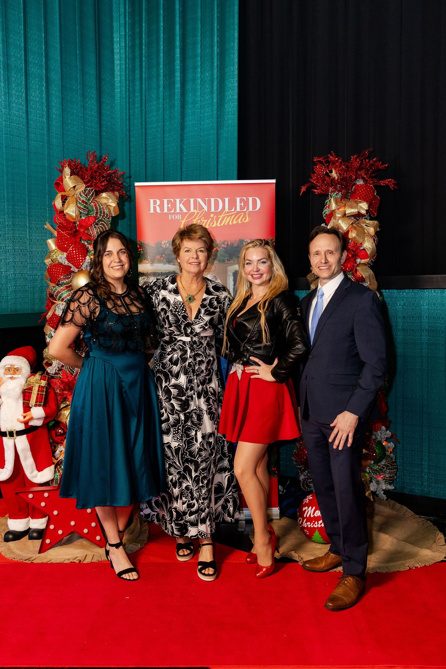 Four guests pose in front of a Rekindled for Christmas movie banner at a festive premiere event.