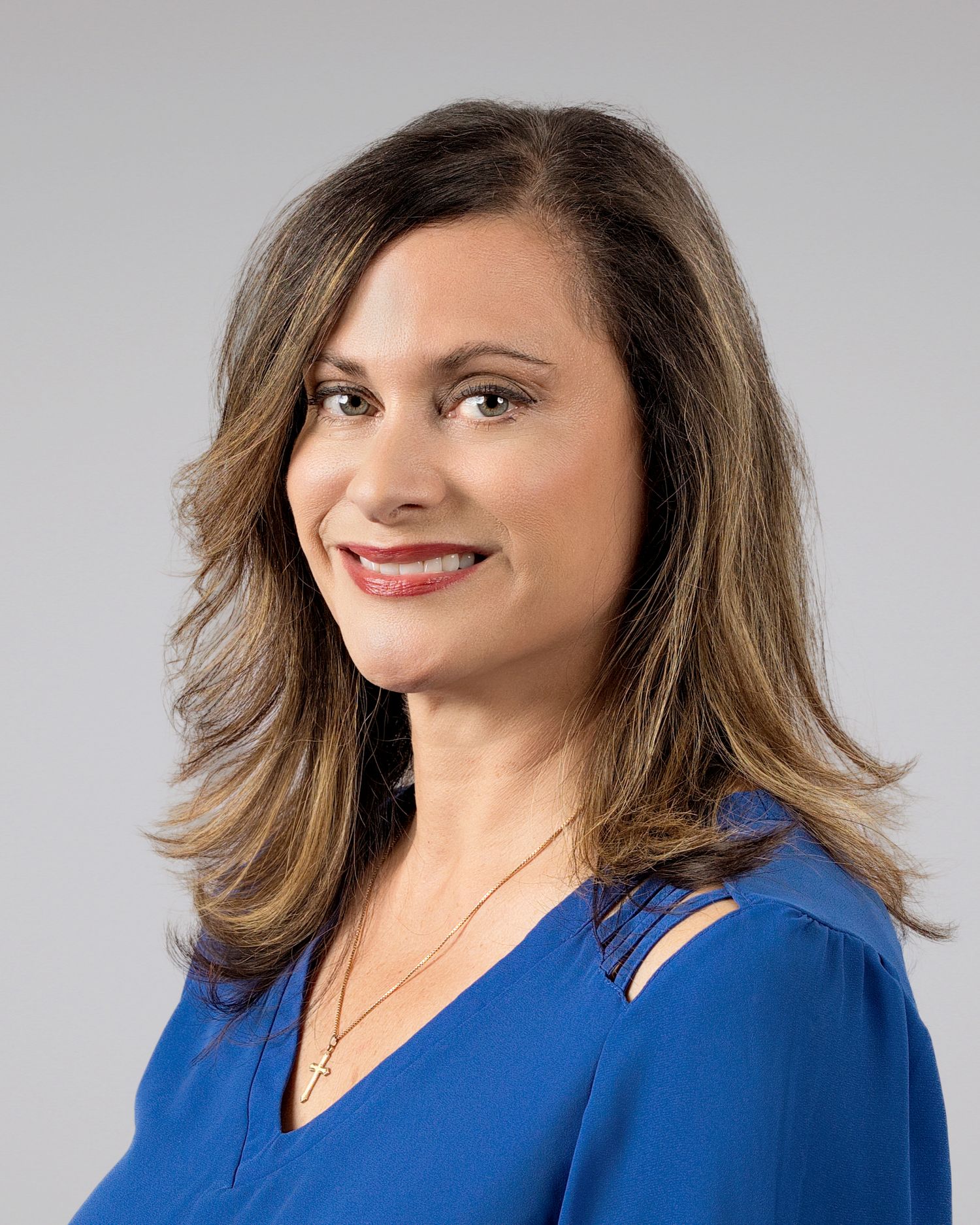Professional woman with brown hair wearing a blue top smiles confidently in a corporate headshot photo.