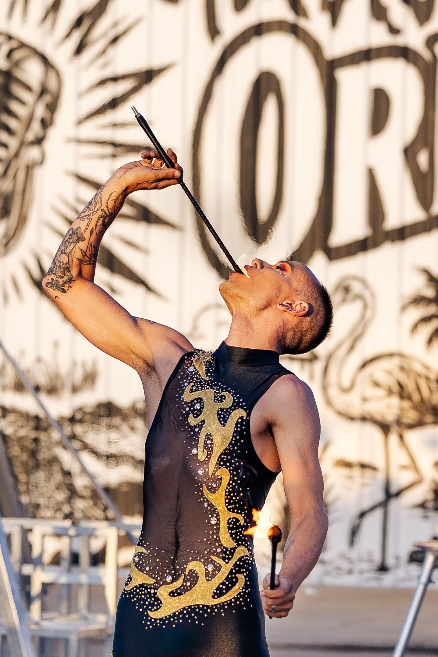 Fire performer in black and gold costume swallowing a sword while holding a torch at an outdoor circus show.