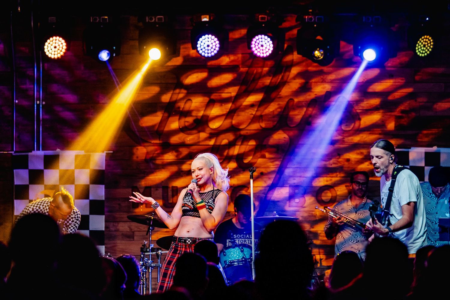 Female vocalist and guitarist performing under colorful stage lights at a live music show.