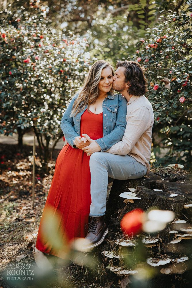 A romantic couple shares an intimate moment amid blooming flowers and trees.