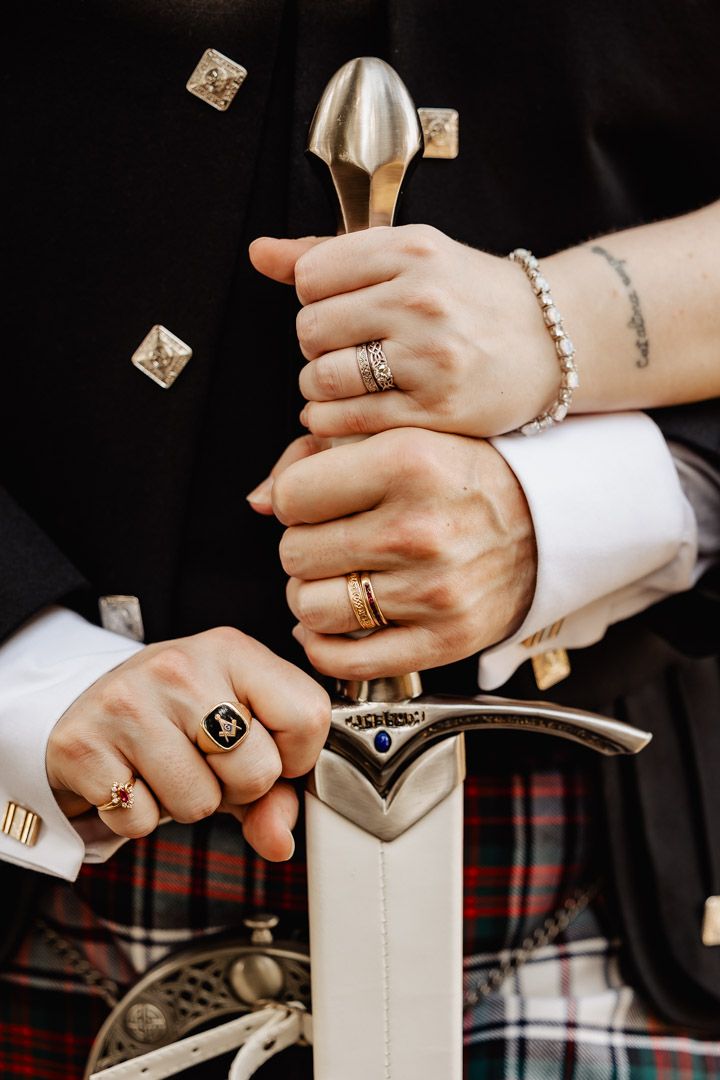 Wedding detail shot of hands holding a ceremonial sword, showcasing rings and Celtic wedding accessories.