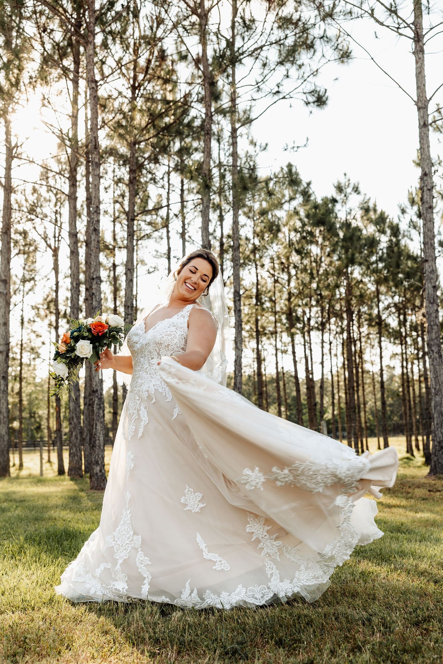 Elegant bride in lace wedding dress twirling in a pine forest with colorful bouquet.