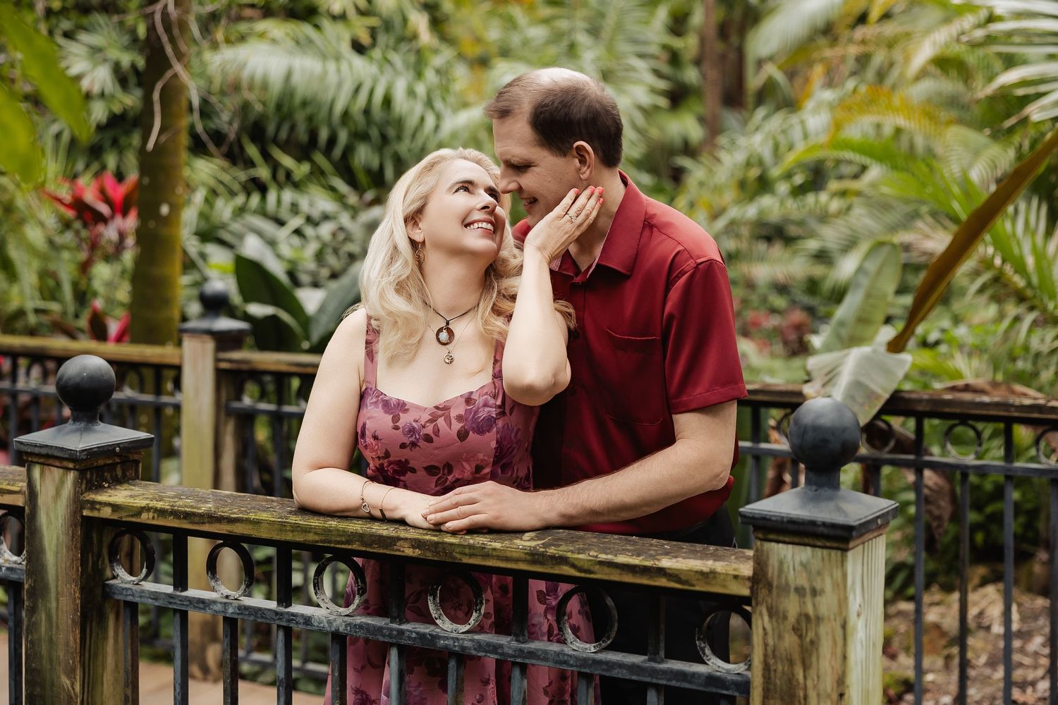 Couple sharing a romantic moment by a decorative fence surrounded by lush tropical greenery.