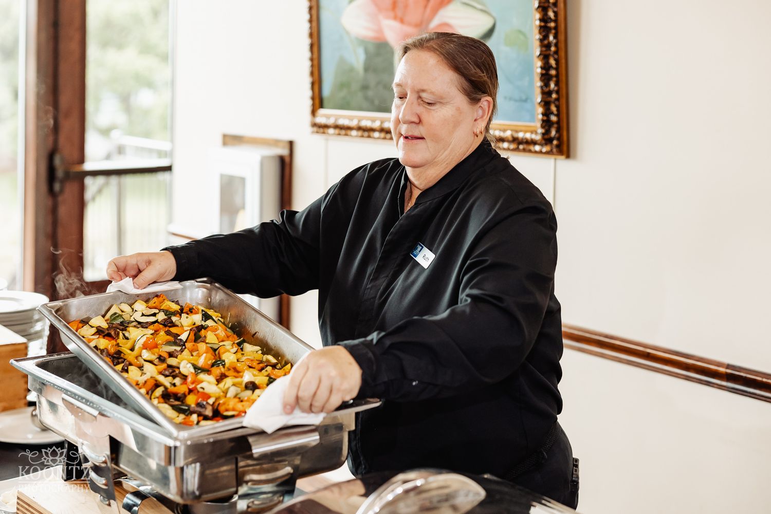Catering staff member serving food from silver chafing dishes at formal event.