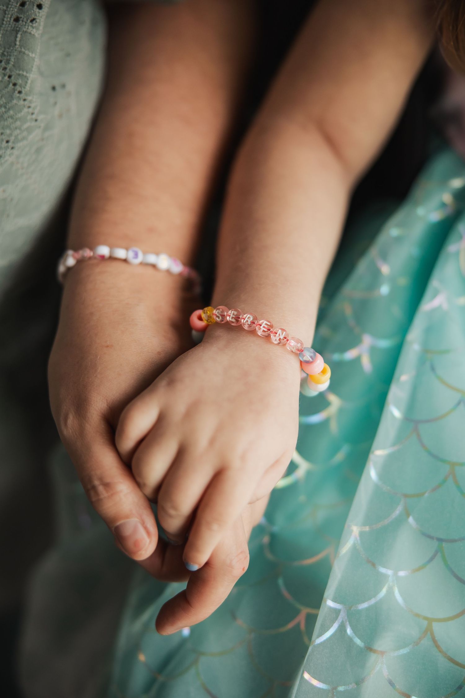 Close-up of two childrens hands wearing colorful beaded bracelets on a teal dress.