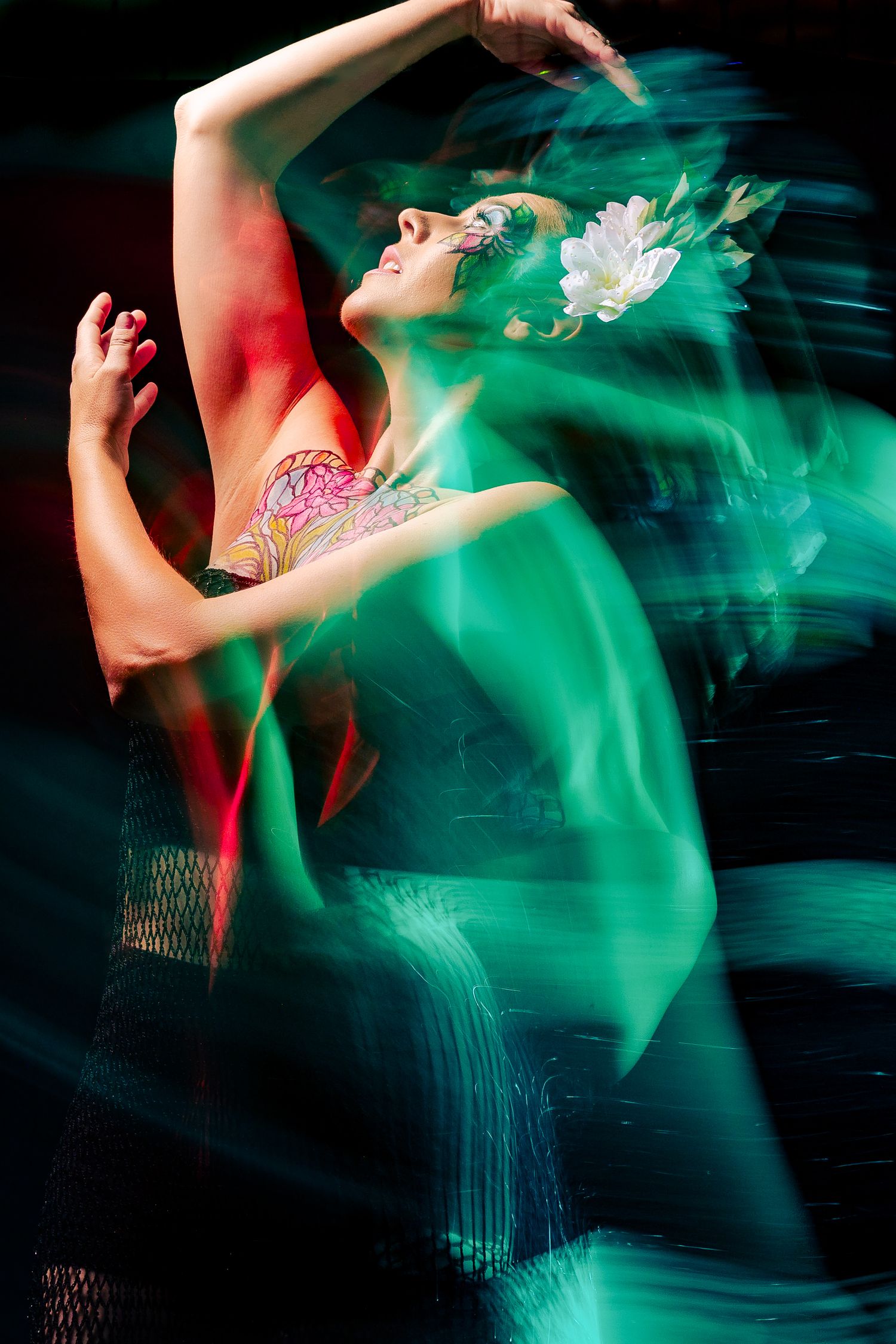 Motion blur long exposure of tattooed dancer in green light with white flower crown on dark background.