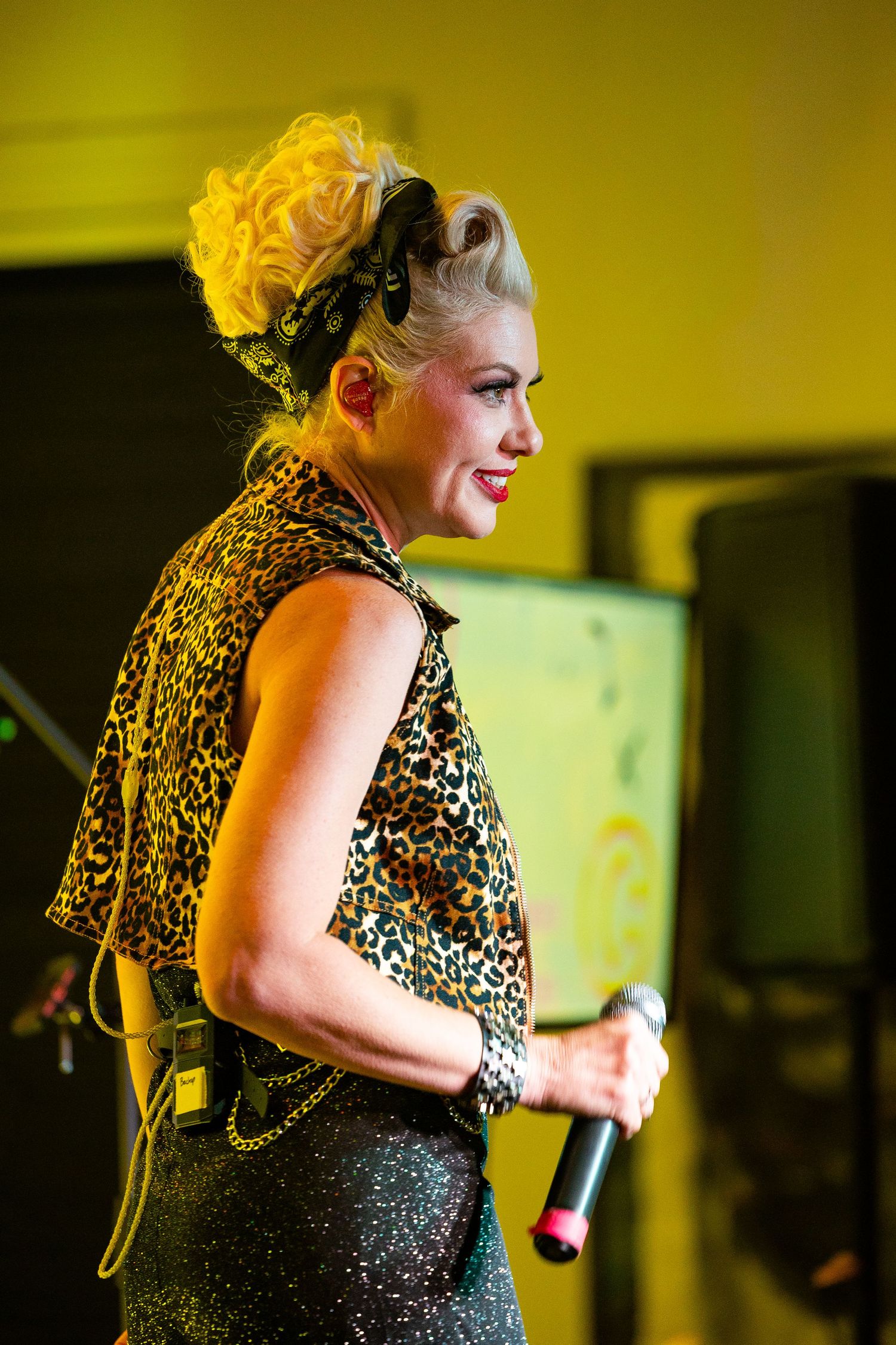A female singer with blonde updo hair wearing leopard print top performs on stage holding a microphone.
