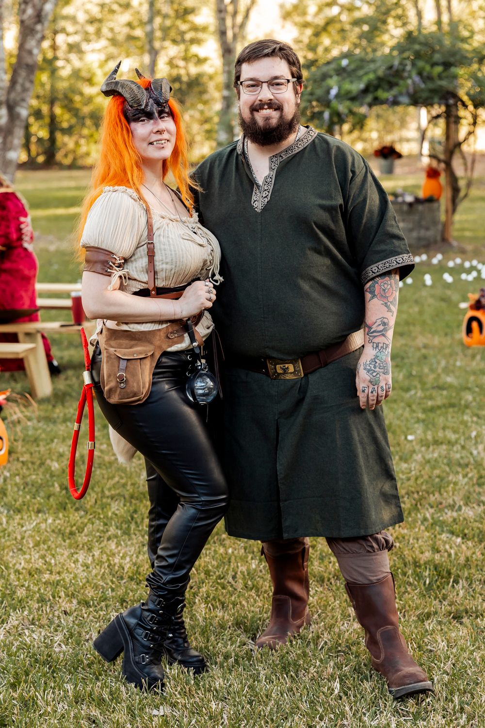 Couple in Renaissance festival costumes pose outdoors, woman in horned headpiece and man in green Viking tunic.