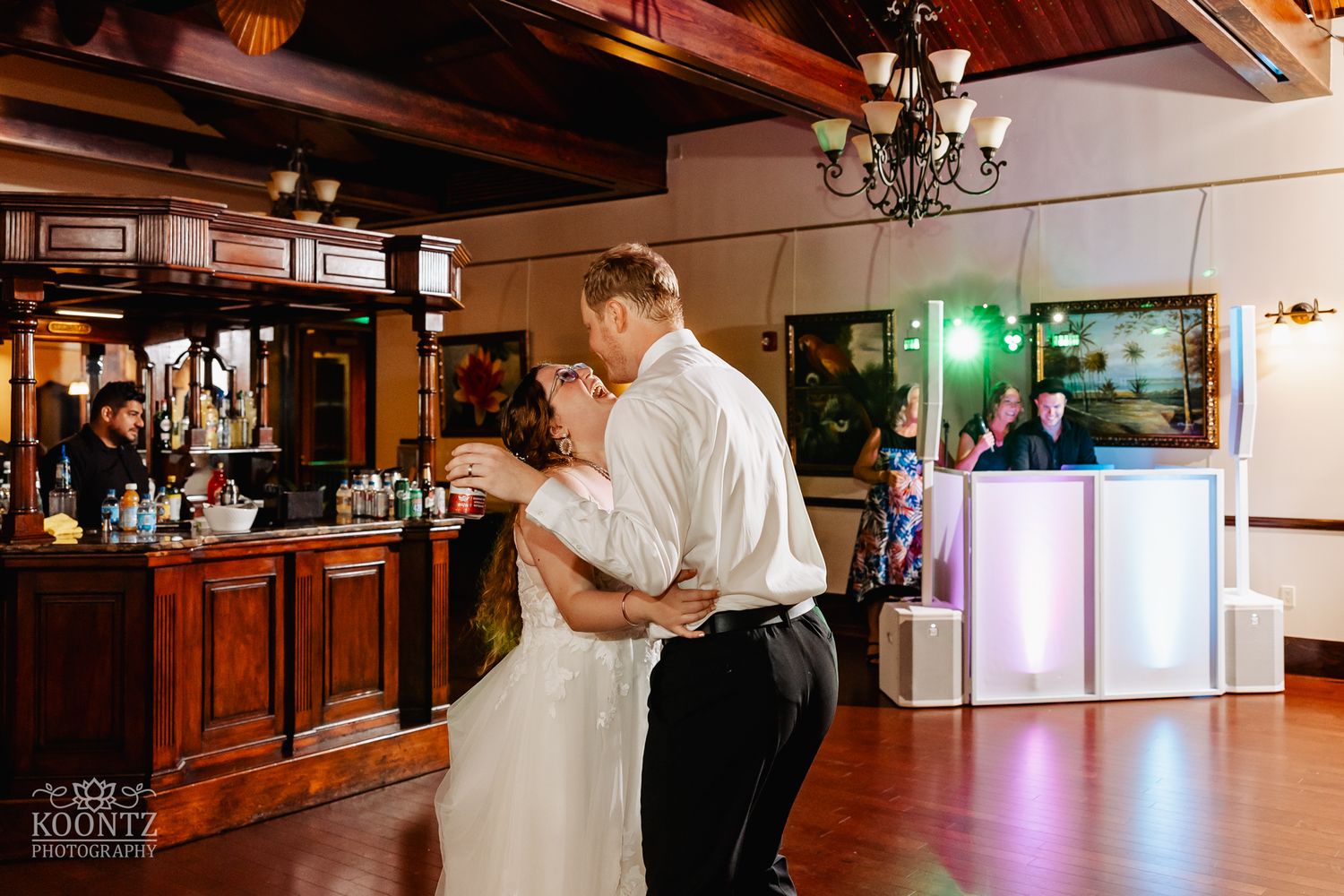 Couple shares an intimate slow dance in an elegant venue with wooden bar and chandeliers.