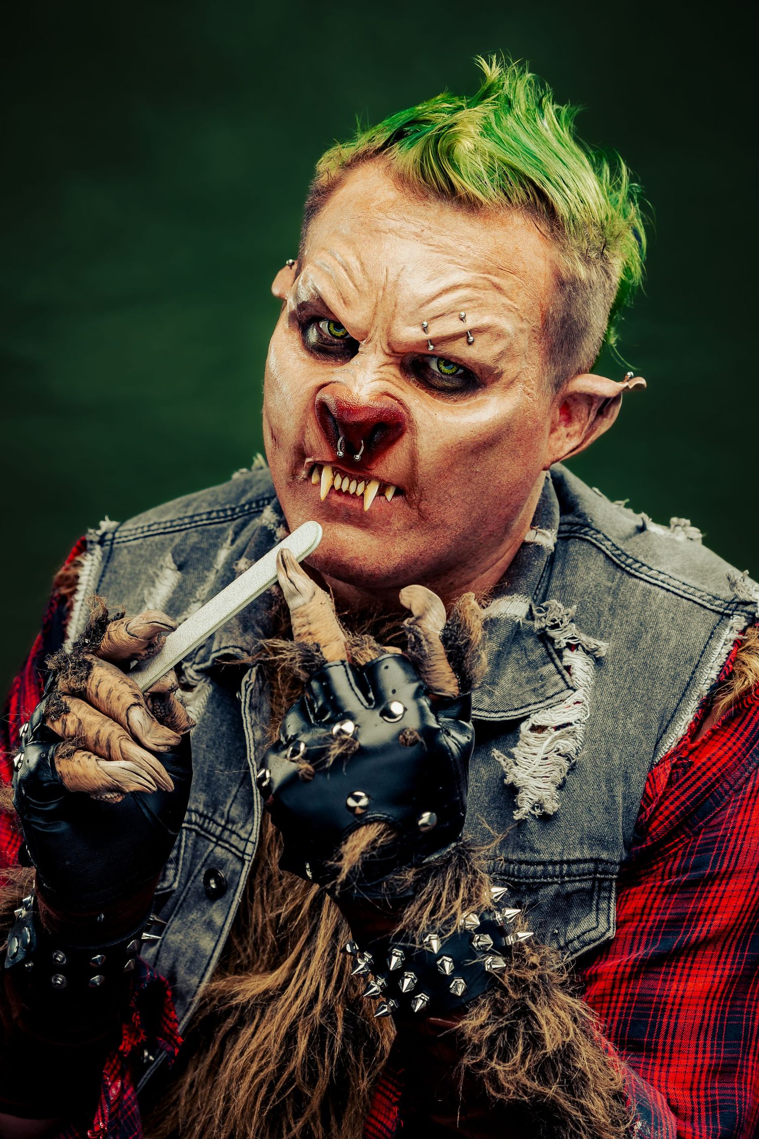 Monster-themed costume with green hair and prosthetic fangs smoking against dark background.