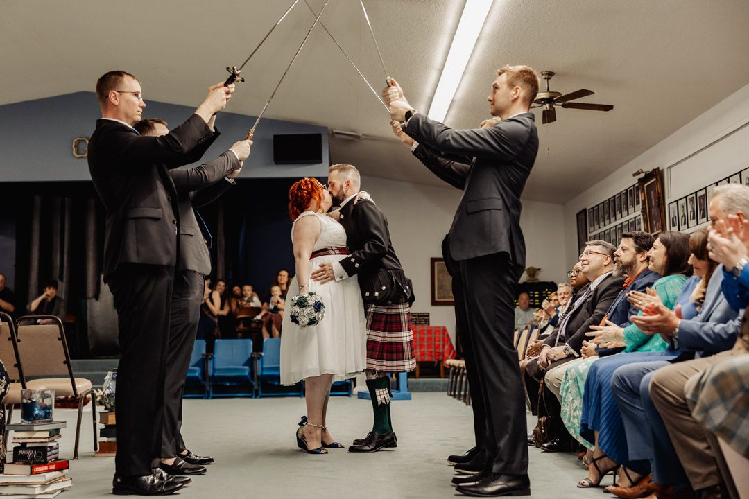 A unique wedding ceremony tradition with groomsmen holding crossed swords over the couple.