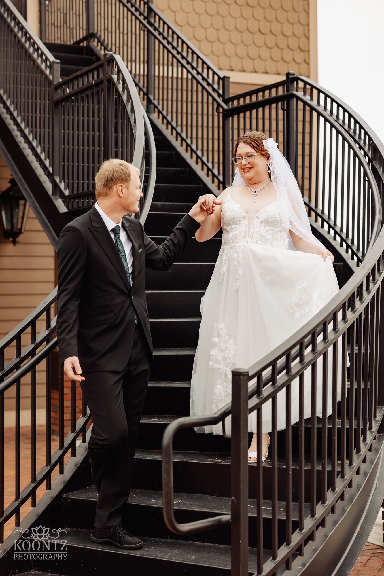 Couple sharing moment on curved staircase with ornate iron railings.