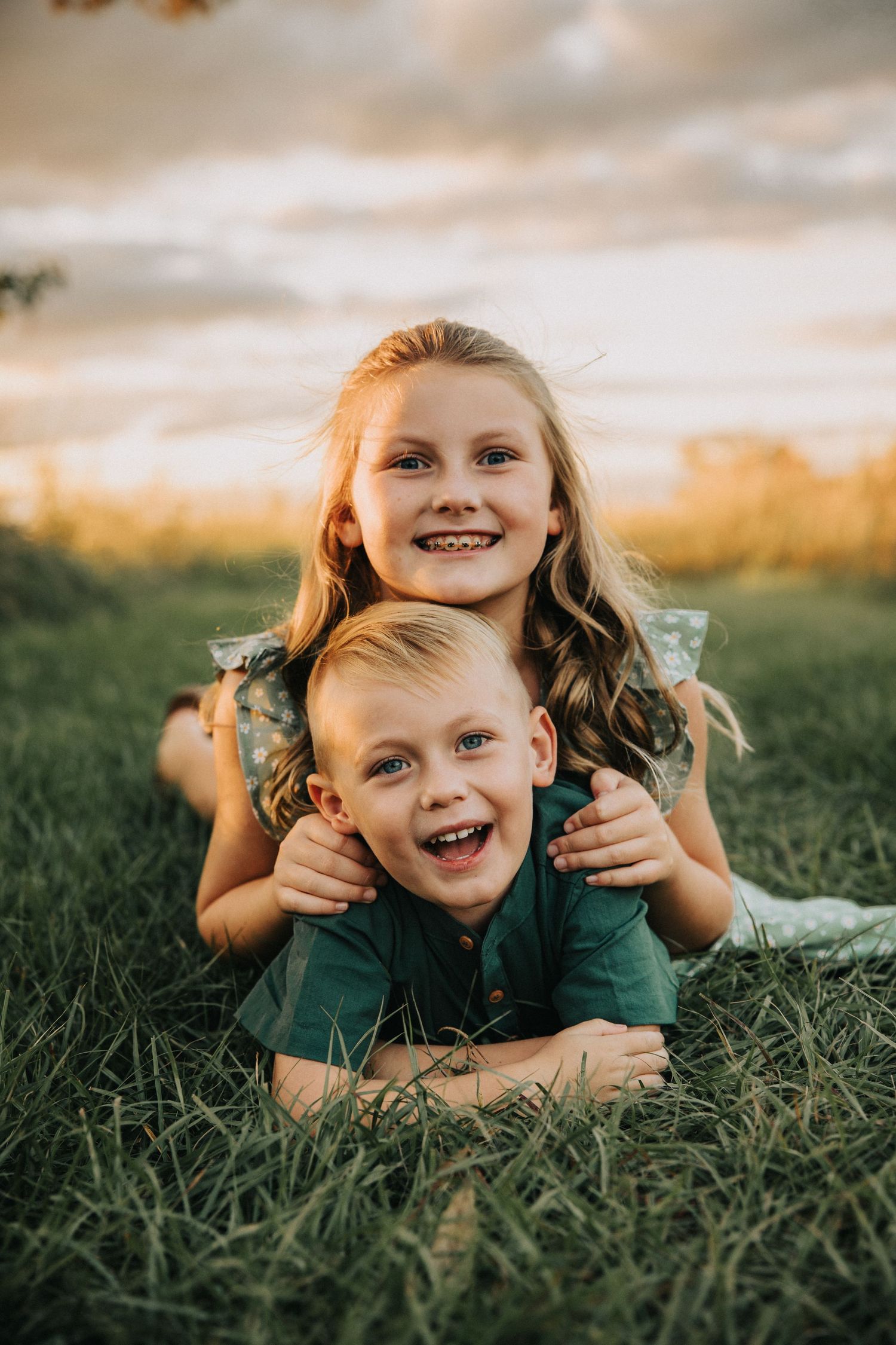 A heartwarming outdoor portrait of two siblings playing together in grass at sunset.