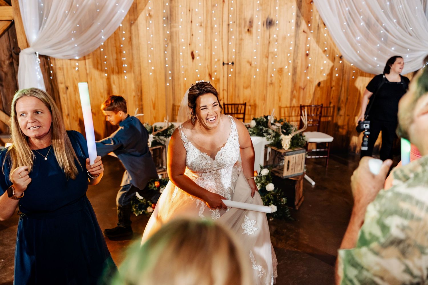 Joyful dancing and celebration during barn wedding reception with white drapes and wooden walls.