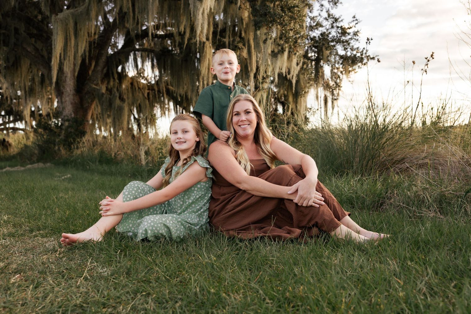 Family enjoying relaxed portrait session in grassy field with Spanish moss trees.
