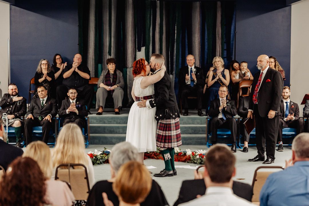 Bride and groom share first kiss at Scottish wedding ceremony as guests applaud.