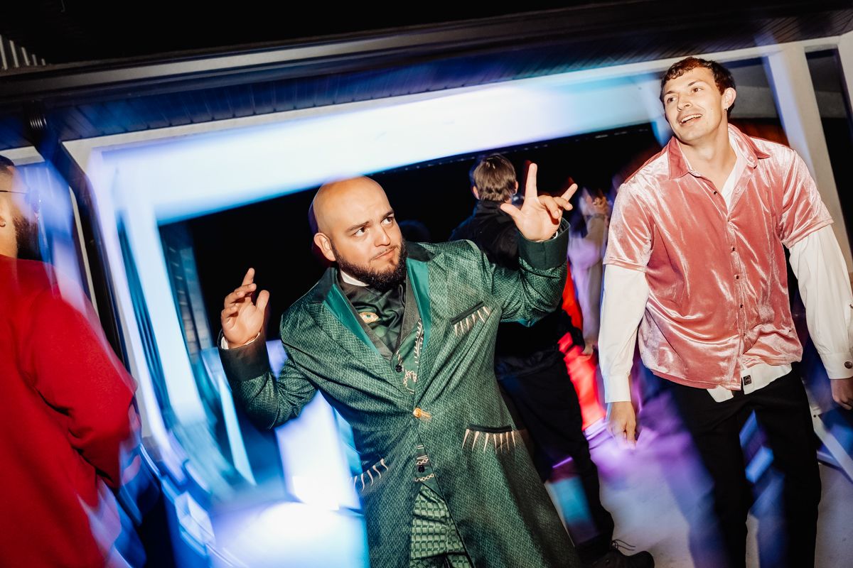 Man in green velvet suit dancing energetically at a colorful wedding reception party.