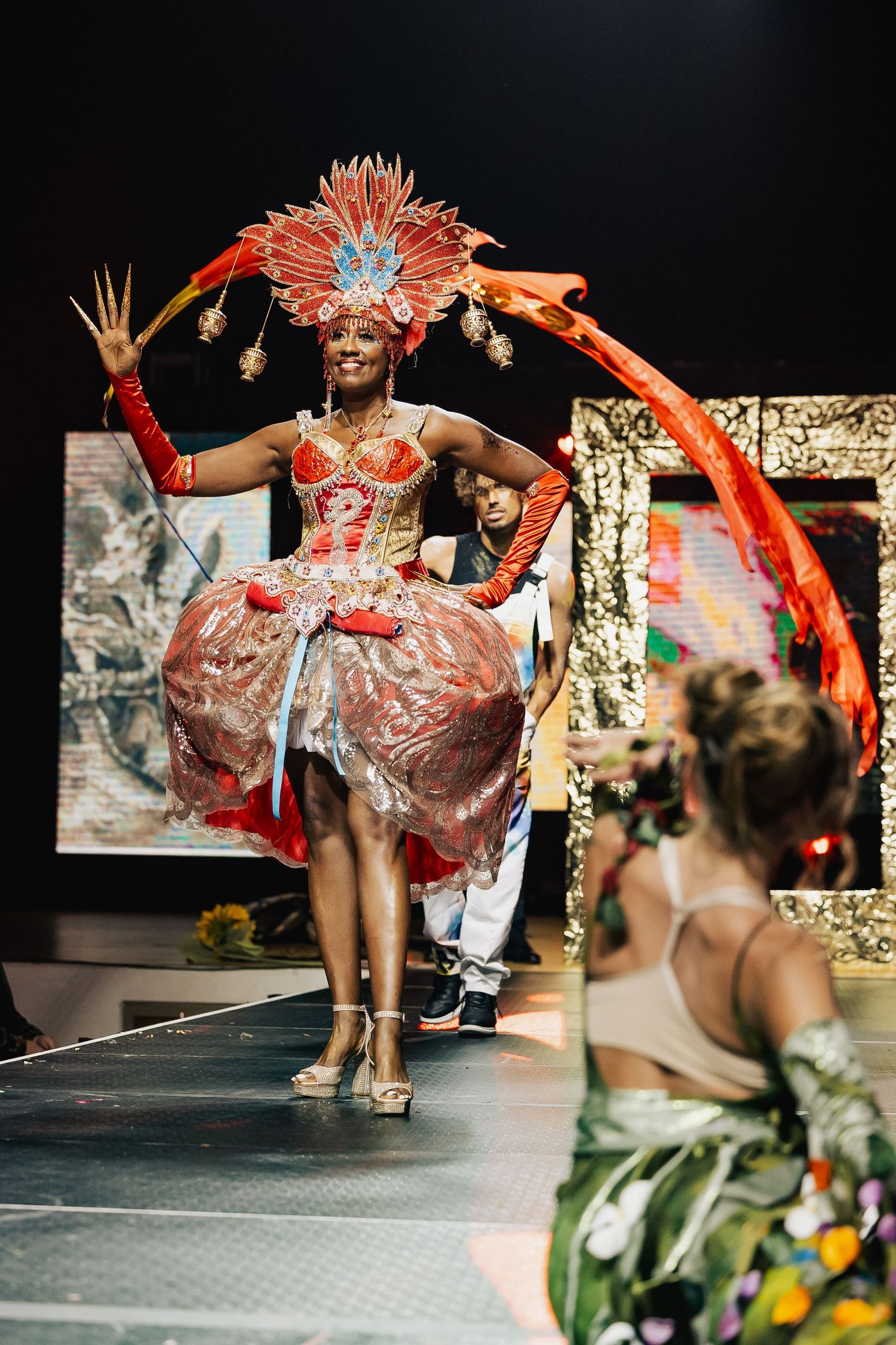Performer in elaborate red carnival costume with feathered headdress dancing on stage.
