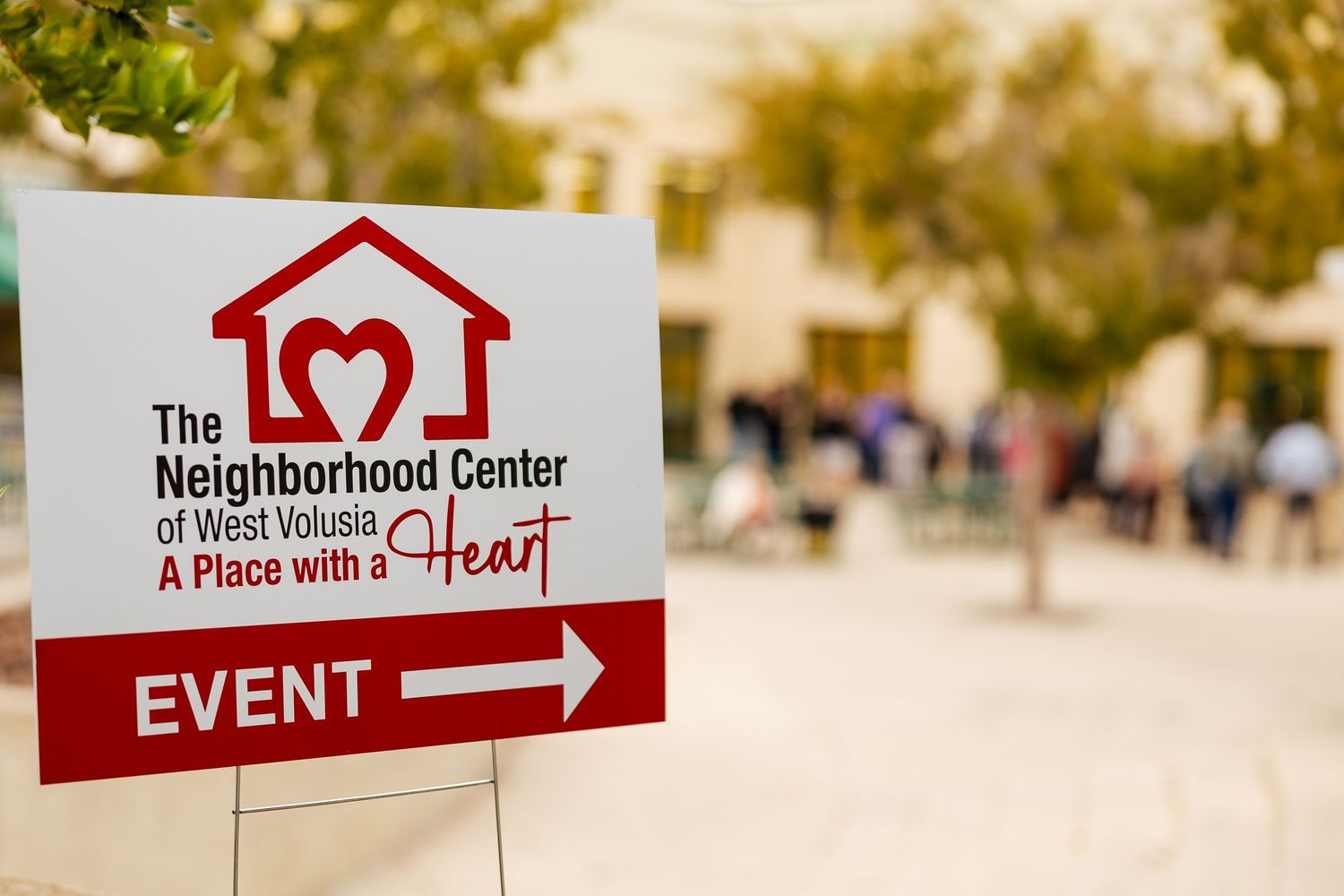 The Neighborhood Center of West Volusia event directional sign displayed outdoors on a sunny day.