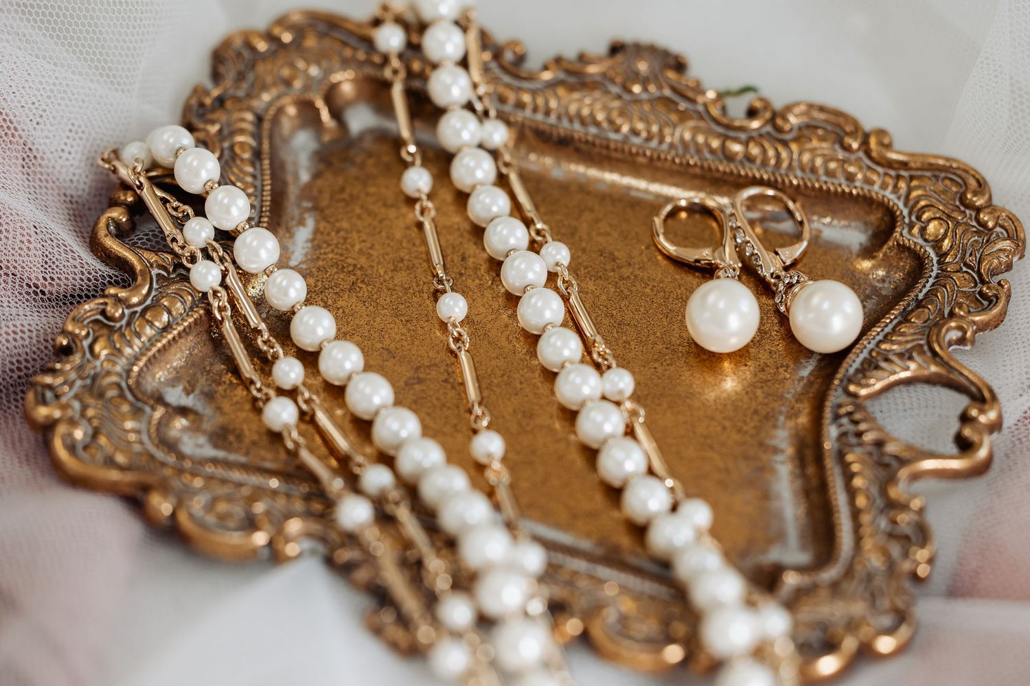 Pearl necklace, bracelet, and drop earrings arranged on an ornate gold vintage tray.