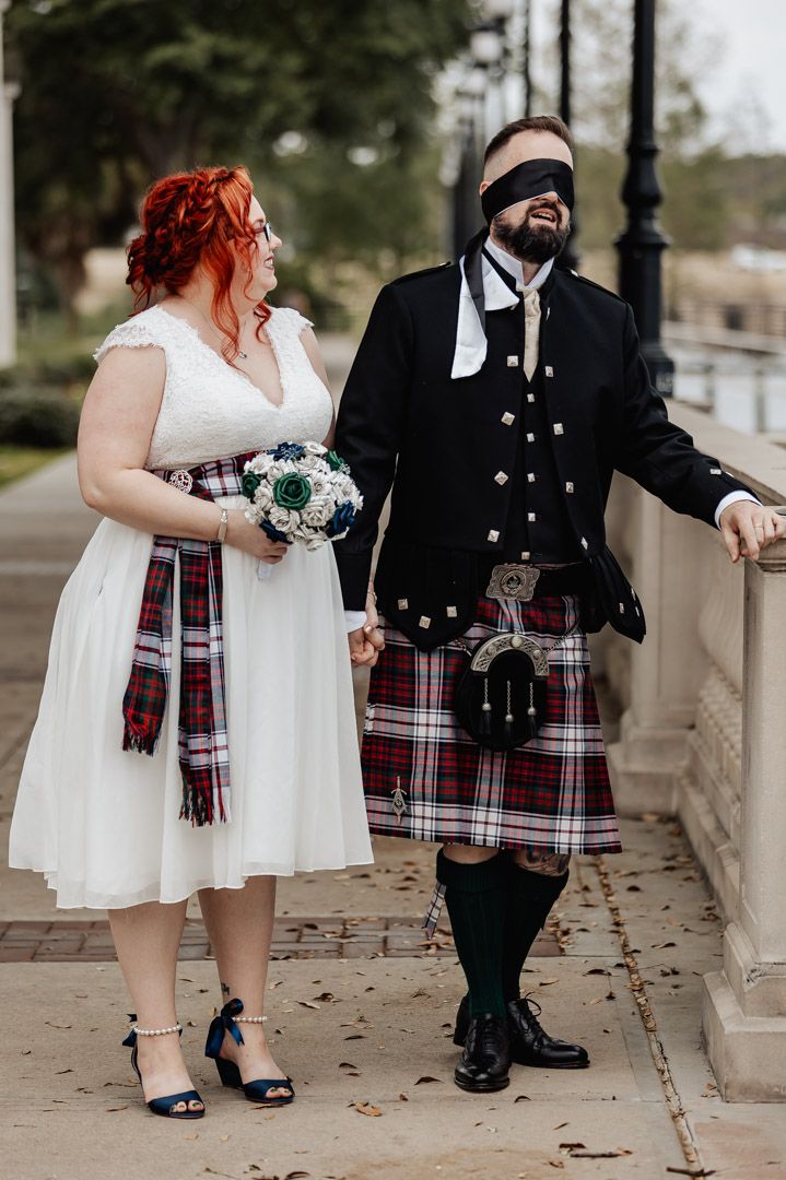 Couple in Scottish wedding attire posing together on a stone walkway.