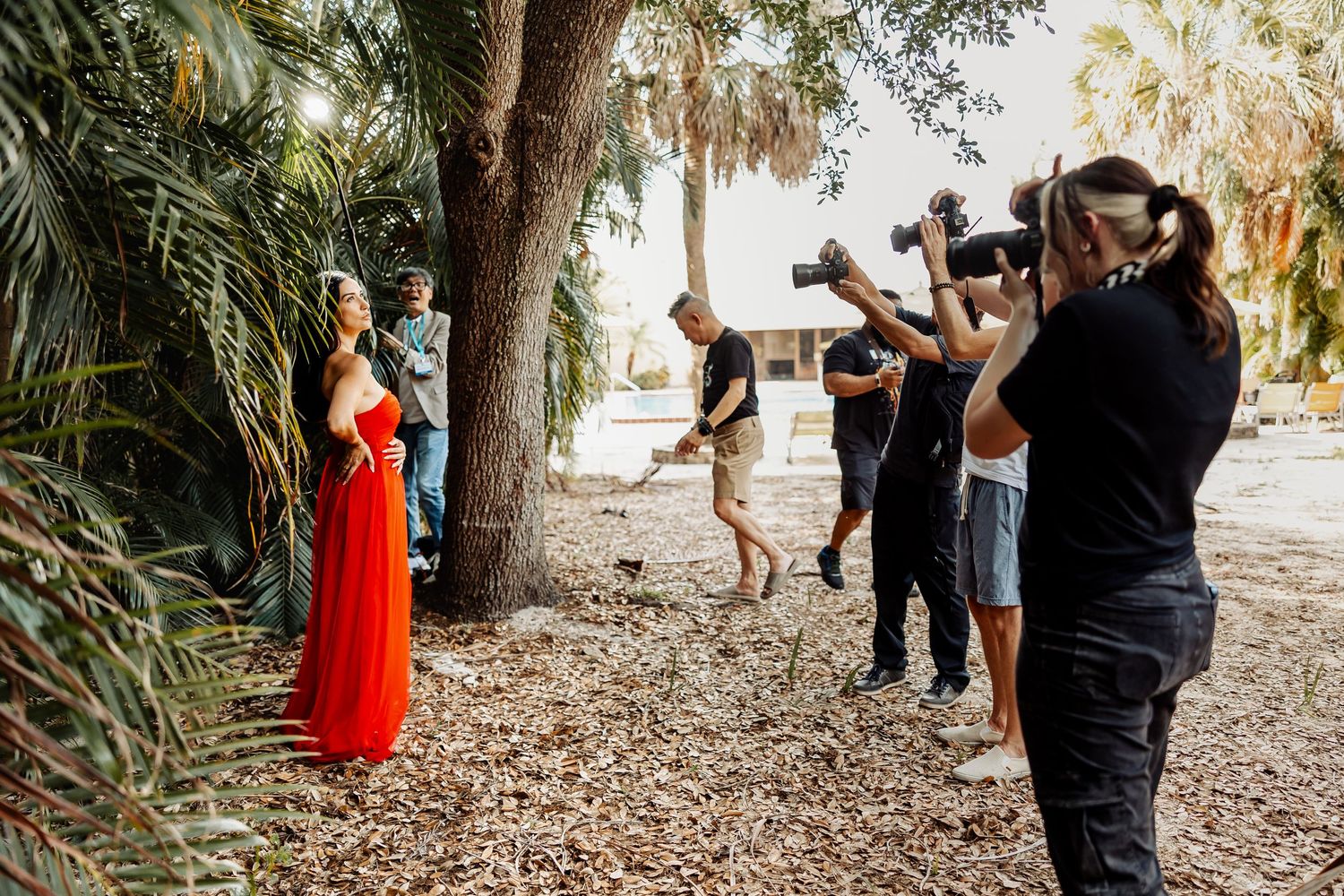 Behind the scenes of photoshoot with multiple photographers capturing model in red dress.