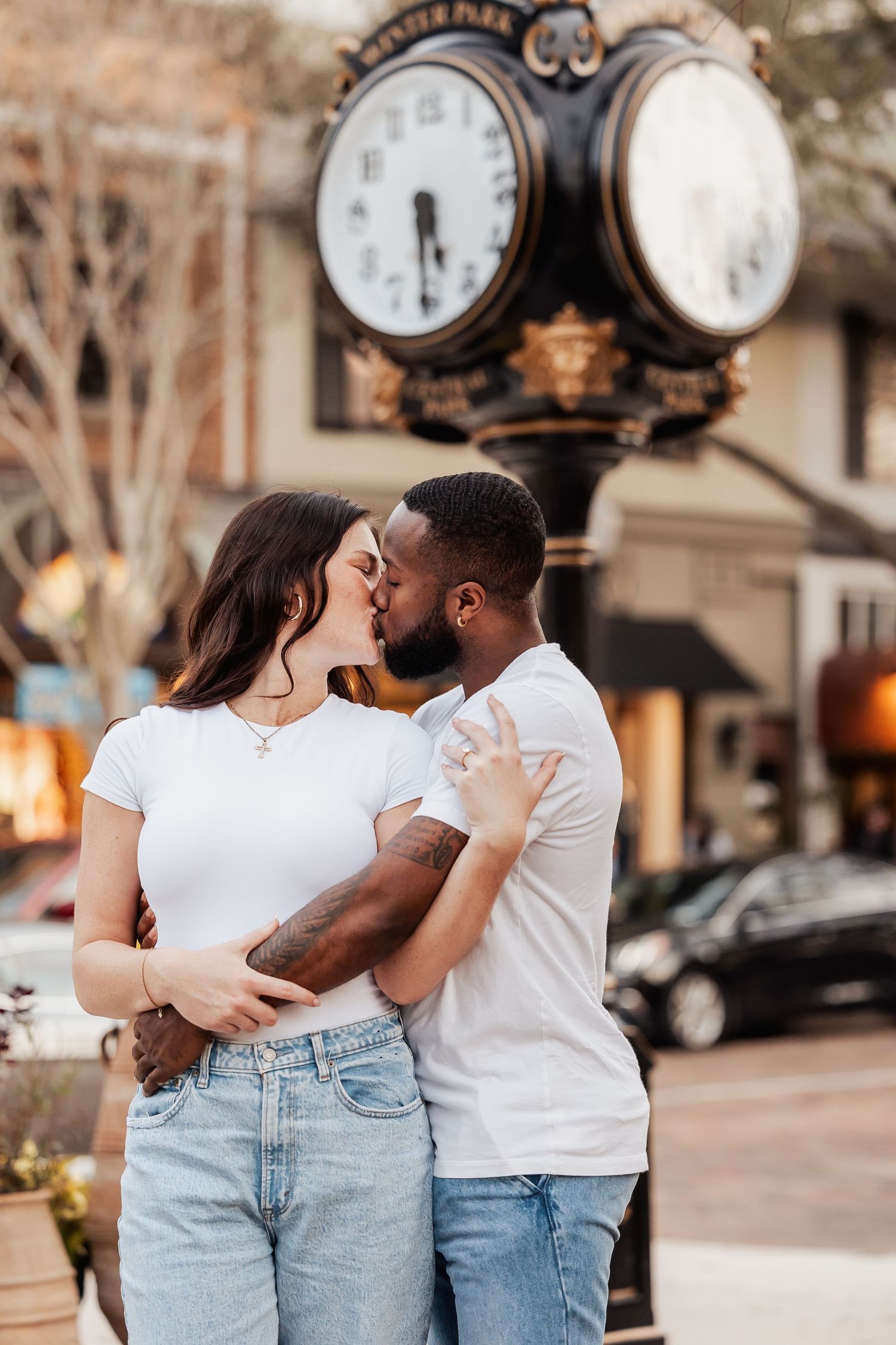 Intimate moment shared between a couple in front of an ornate street clock during sunset.