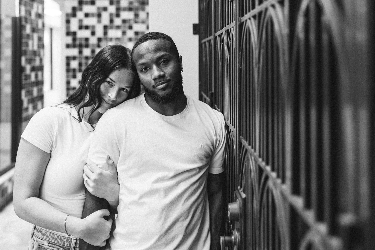 Black and white portrait of couple sharing intimate moment by metal railing.