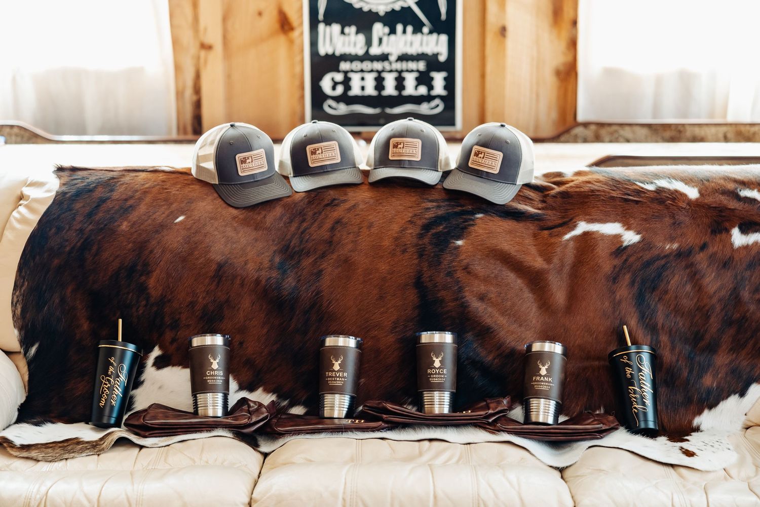 Brown cowhide display with trucker hats and 'CHILI' text sign in rustic wooden setting.